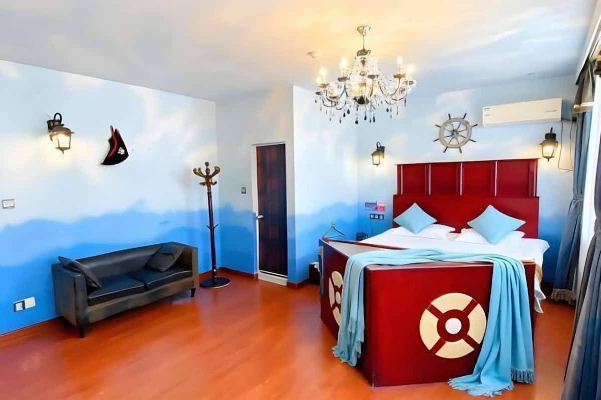 Une chambre à coucher avec une tête de lit rouge, un lit recouvert de draps blancs, un canapé noir et un plancher en bois.