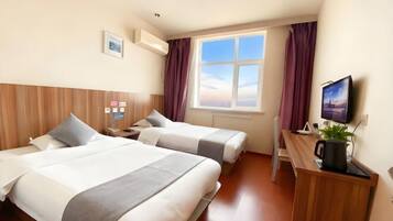 Ein Hotelzimmer mit zwei Betten, einem Schreibtisch, einem Fernseher und einem Fenster mit Vorhängen.