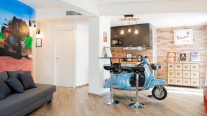 Ein modernes Wohnzimmer mit einem grauen Sofa, einem blauen Roller und einer Küchenzeile mit Backsteinwand und Holzschränken.