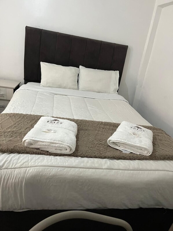 Un lit bien fait, avec des draps blancs, deux oreillers et deux serviettes pliées posées sur une couverture marron.