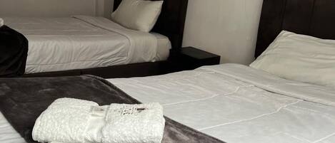 A hotel room with two beds, each with a dark headboard and white bedding. A folded towel is placed on the bed in the foreground.
