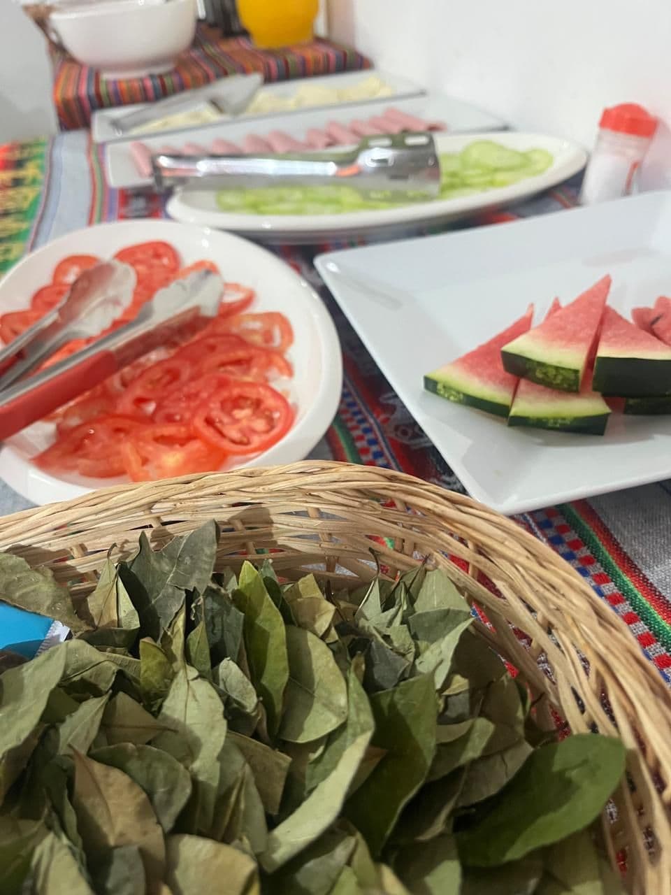A table with various food items including sliced tomatoes, watermelon, and a basket of dried leaves.