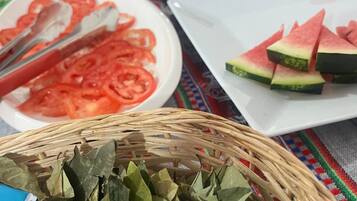 A table with various food items including sliced tomatoes, watermelon, and a basket of dried leaves.