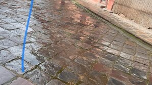 Een binnenplaats met stenen bestrating, planten in potten, en gebouwen met rode deuren en balkons.