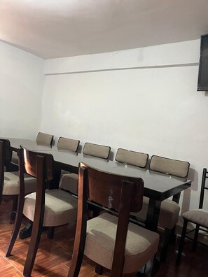 A conference room with a long table and six chairs, a white wall, and a mounted television. - Enede Hostel Cusco (Cusco)