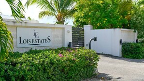 A sign for Lois Estates with a gated entrance, surrounded by lush greenery and palm trees. - Lois Estates: 1 bedroom home (Long Bay Caicos Islands)