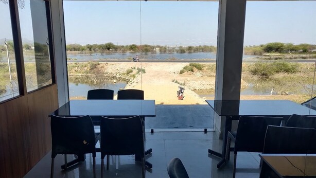 Una habitación con un ventanal grande que da a una carretera y una masa de agua. Hay mesas y sillas dispuestas para comer.