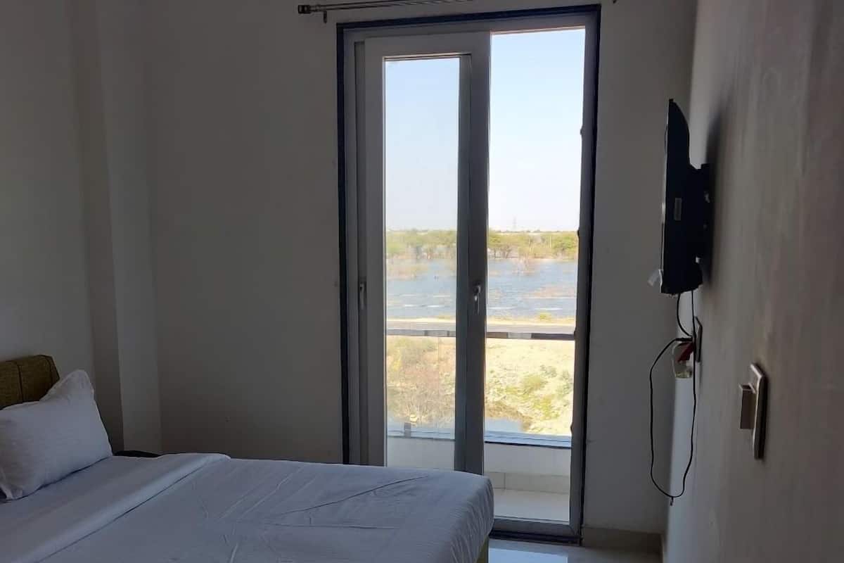 Ein Schlafzimmer mit einem Bett, einer Klimaanlage, einem an der Wand montierten Fernseher und einer Glastür, die auf einen Balkon mit Blick auf ein Gewässer führt.