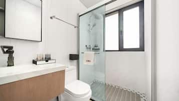 A modern bathroom with a glass shower enclosure, a white toilet, and a wooden vanity.