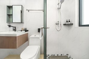 A modern bathroom with a glass shower enclosure, a white toilet, a wooden vanity, and a small shelf with toiletries. - Shanghai Red Carp Business Hotel (Zhujiajiao Scenic Area Ancient Town) (Shanghai)