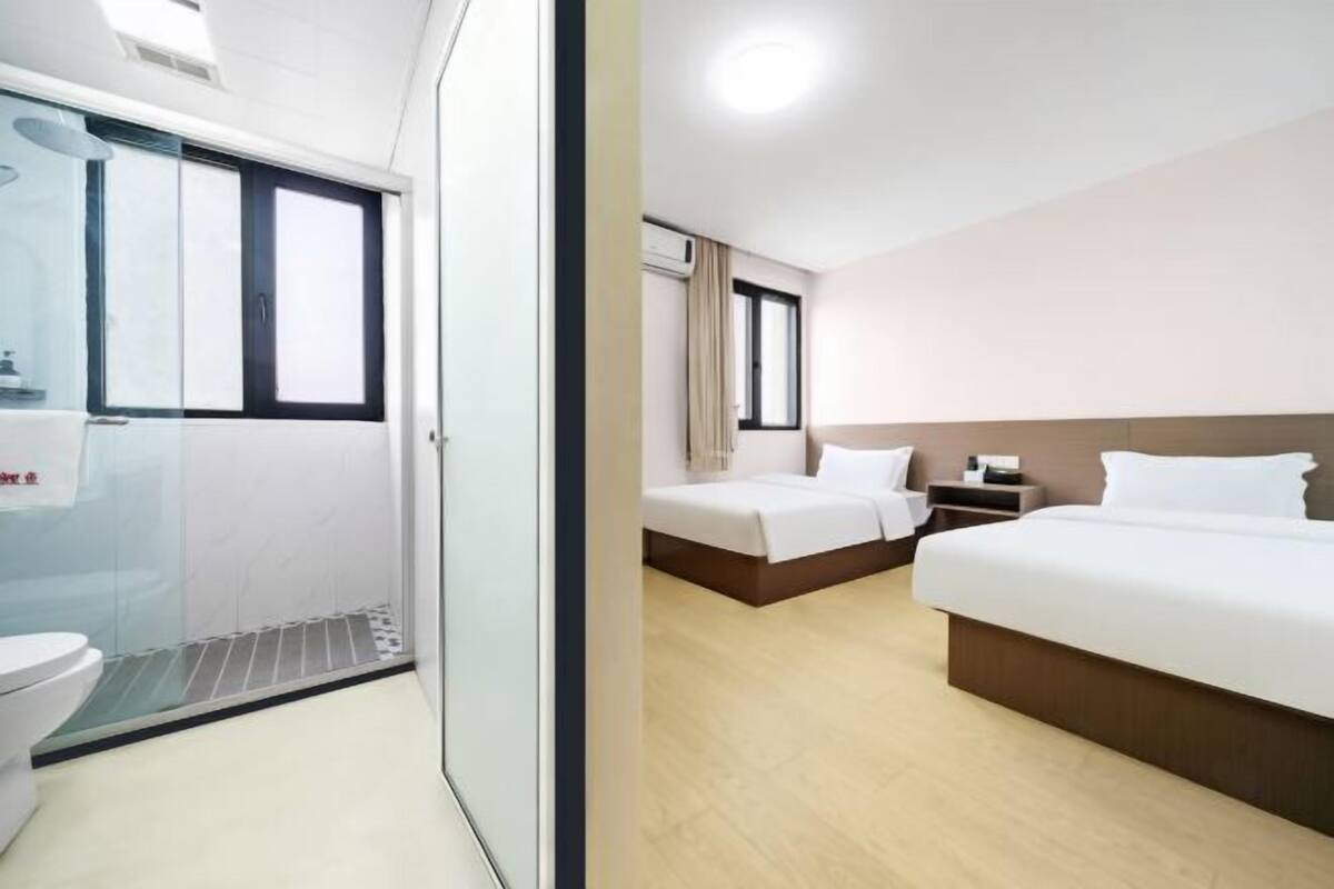 A hotel room with two beds, a bathroom, and a glass shower enclosure.