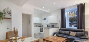 A modern living room with a leather sofa, a dining table with chairs, and a kitchen in the background.