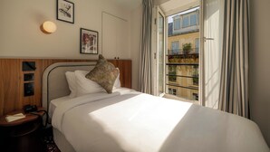 A hotel room with a bed, a bedside table with a phone and notepad, a wall-mounted light, and a window with curtains. - SALVIA Paris (Paris)