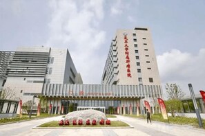 A modern building with a prominent entrance, a large rock sculpture in the foreground, and red banners.