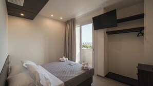 A modern hotel room with a bed, a flat-screen TV mounted on the wall, a balcony with a view, and a small desk area. - Residence Hotel Goldoni6 (Rimini)