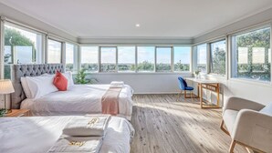 Un dormitorio moderno con dos camas, un escritorio y ventanas amplias que ofrecen vistas al paisaje.