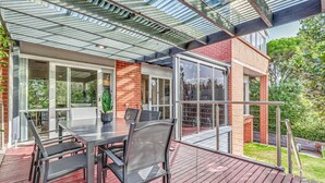 Un patio techado al aire libre con una mesa y sillas, una planta en maceta y vista a un edificio de ladrillo.
