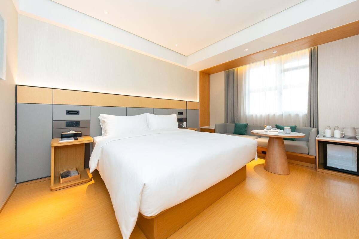 A modern hotel room with a large bed, a desk, a chair, a small table, and a TV.