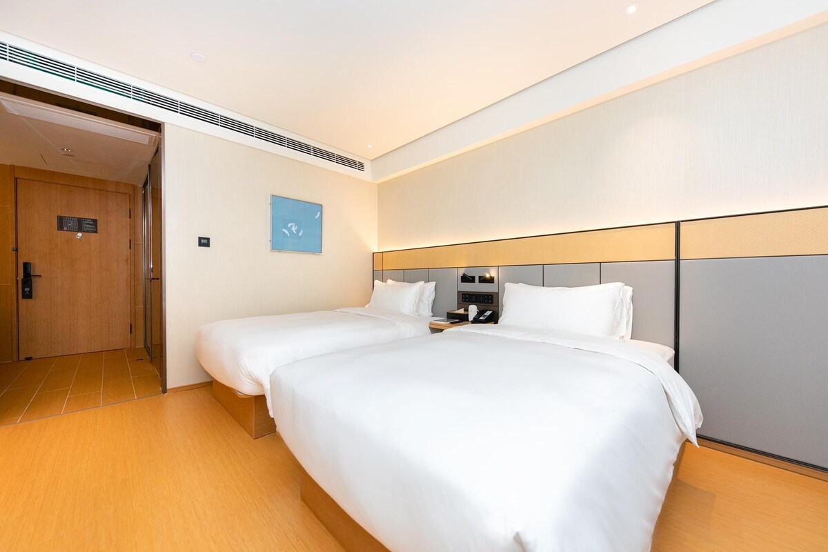 Habitación de hotel con dos camas, piso de madera, teléfono en la pared y una puerta con un cartel.