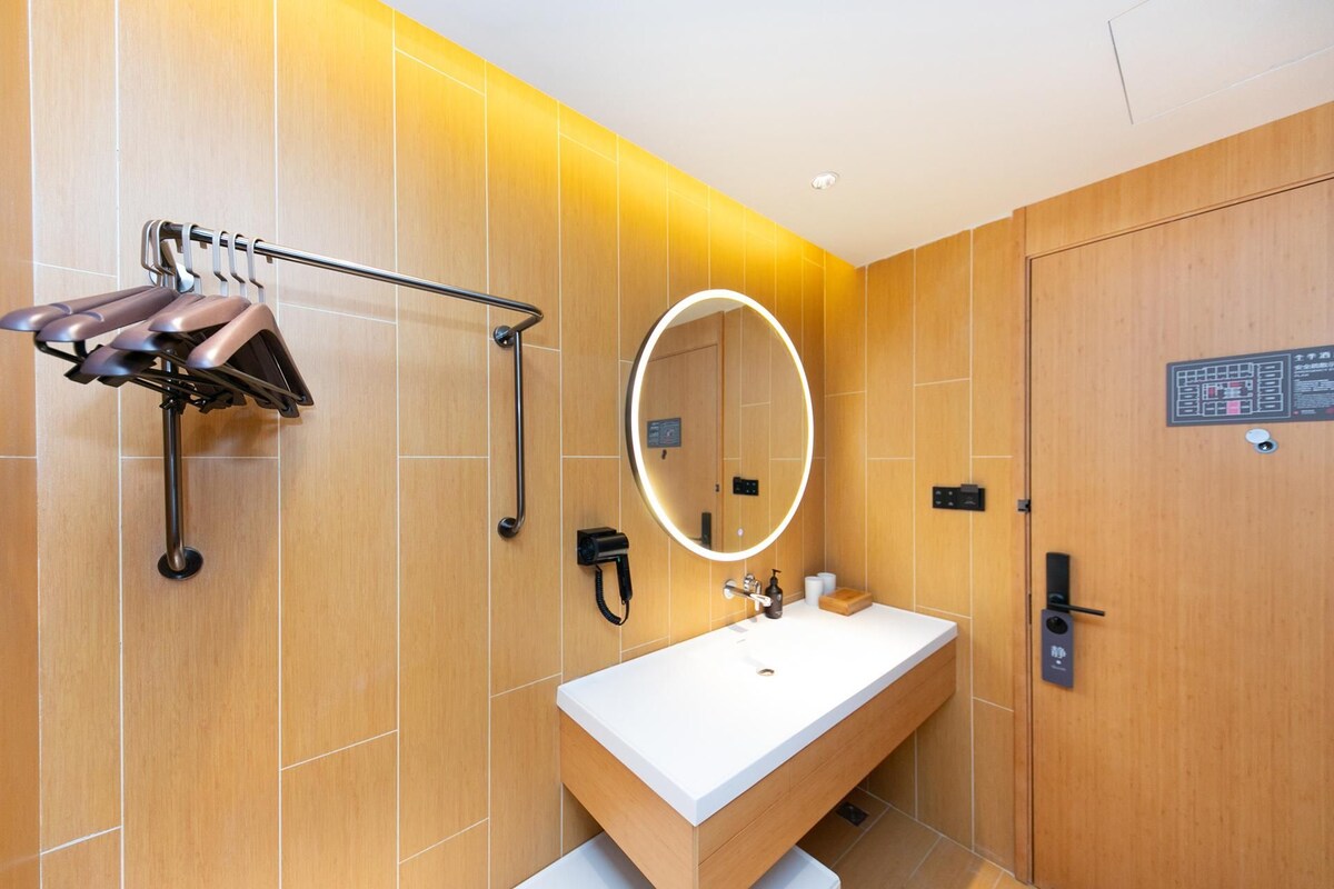 A modern bathroom with a wooden vanity, a round mirror with LED lighting, a towel rack, and a door with a sign.
