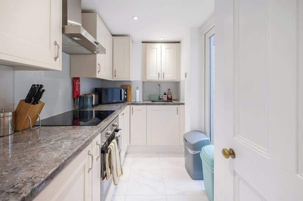 A compact kitchen with white cabinets, a granite countertop, and a stainless steel range hood.
