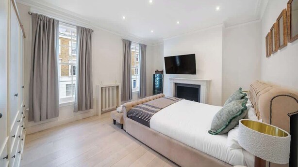 A bedroom with a bed, a TV mounted above a fireplace, and a window with curtains. - New stylish 3-Bed Pimlico House near Big Ben (London)