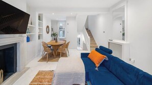 A modern living room with a fireplace, a blue sofa, and a dining area with a round table and chairs. - New stylish 3-Bed Pimlico House near Big Ben (London)