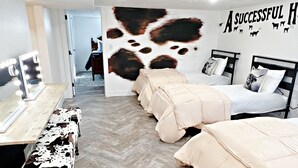 A room with two beds, a vanity with lights, and a wall with a cow print and 'A SUCCESSFUL HOME' text.