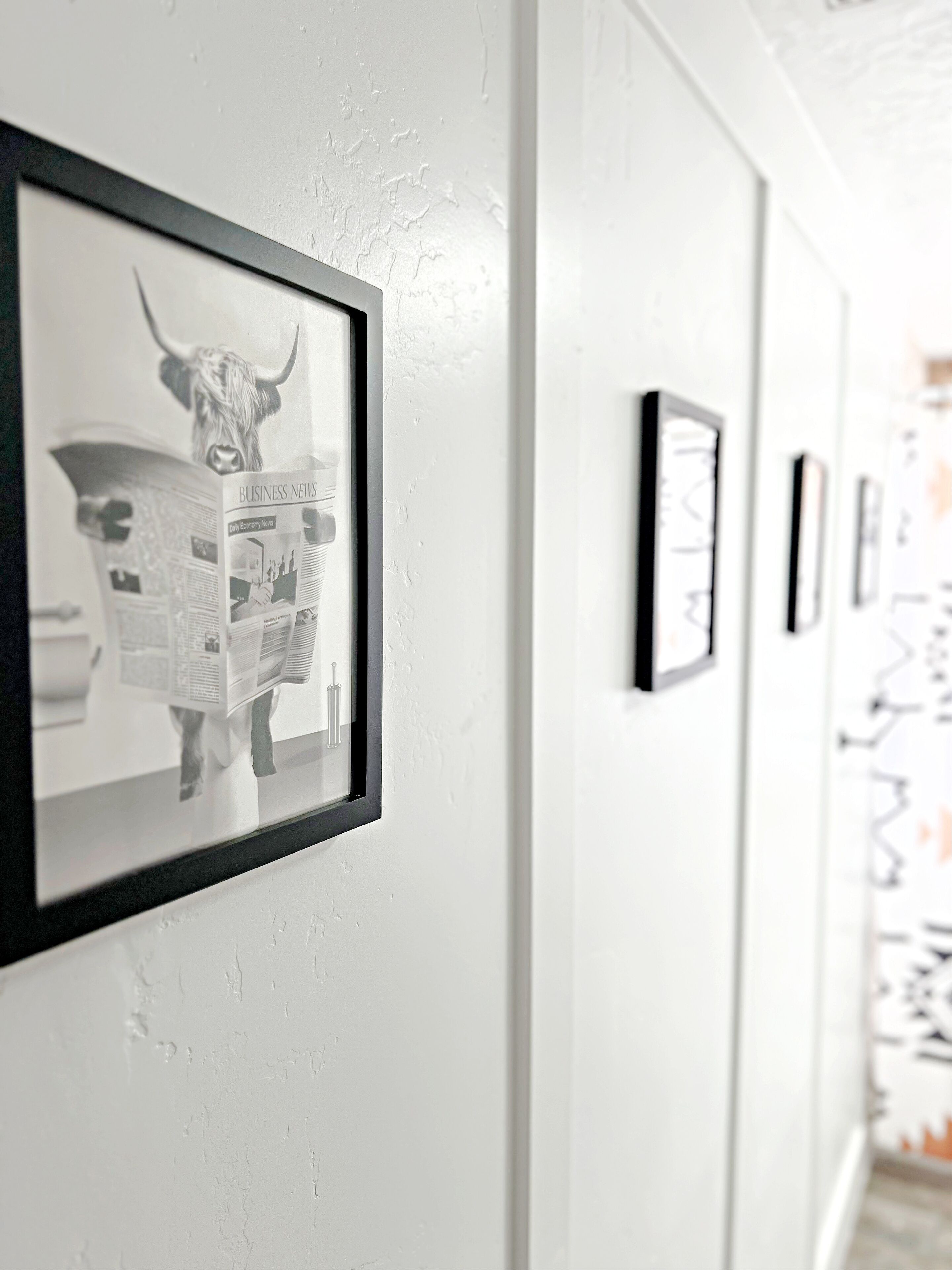 A hallway with framed artwork on the walls, including a bull and a newspaper.