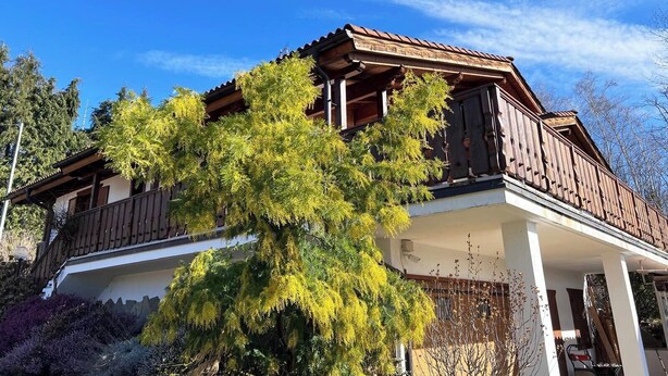 A two-story building with a balcony, surrounded by trees and shrubs.