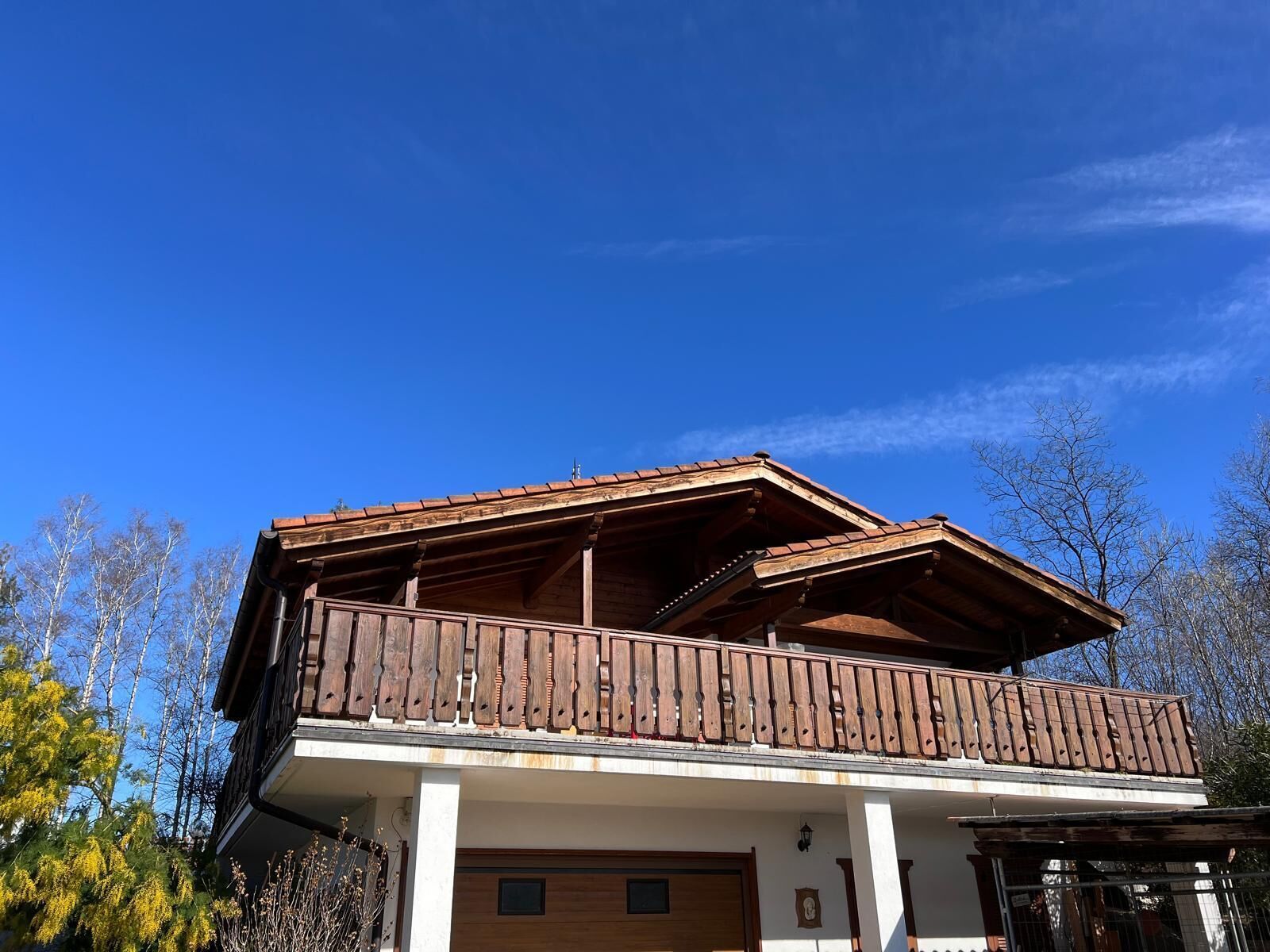 A two-story building with a wooden balcony, a garage, and a clear blue sky.