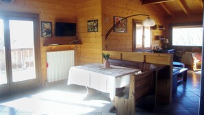A wooden cabin interior with a dining table, chairs, a television, and a window.