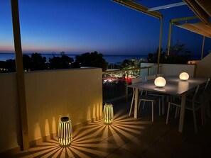 An outdoor patio with a table and chairs, two decorative lights, and a view of the sea at dusk. - Ático-duplex Lagos del Castillo (Denia)