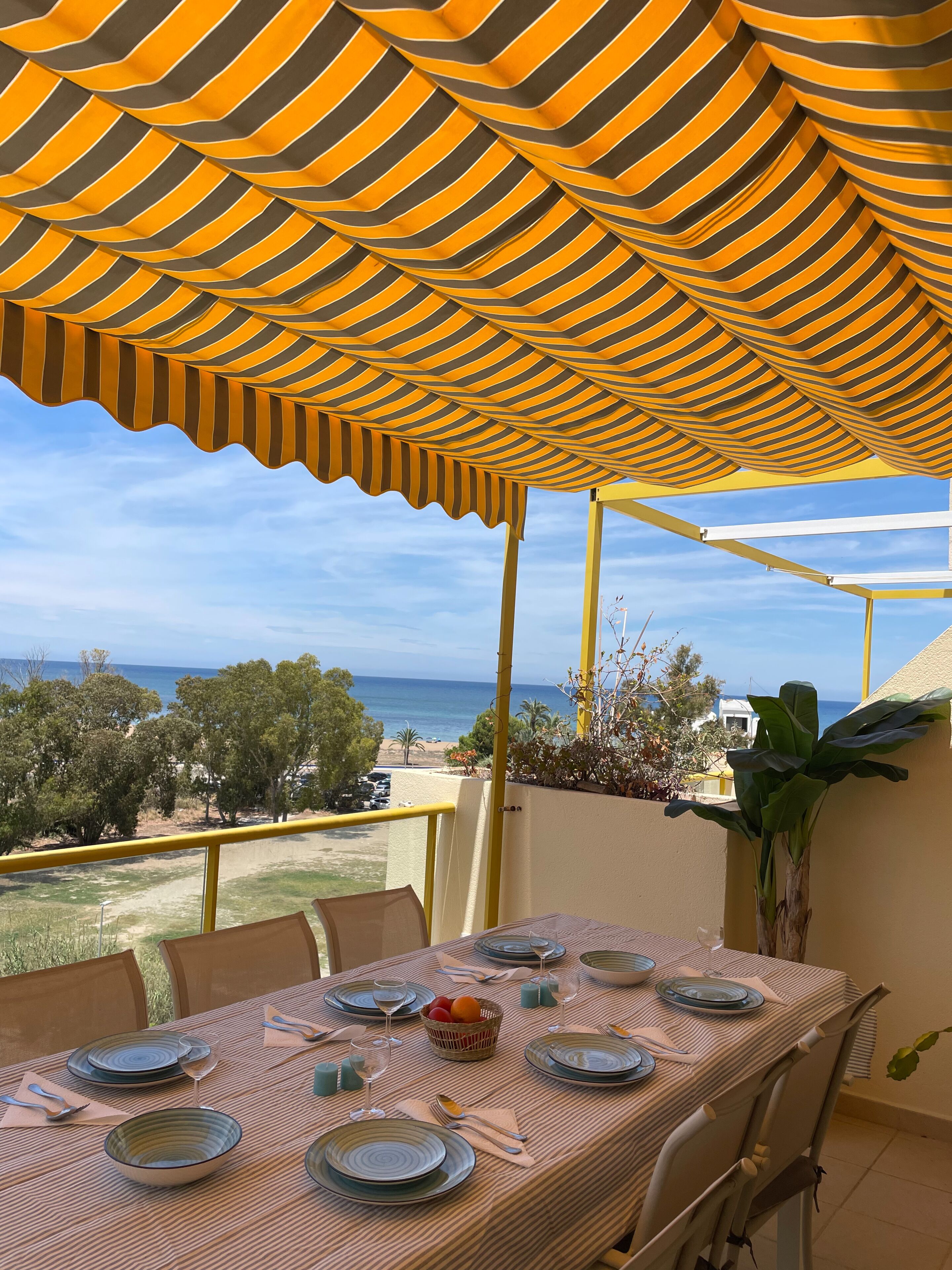 A dining area with a table set for four, overlooking a beach and ocean.
