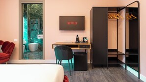 A modern hotel room with a bed, a desk with a computer, a TV, and a walk-in closet with hanging clothes. - My Rooms in Vatican City (Rome)