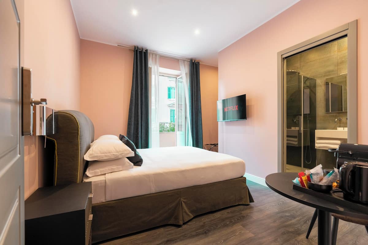 A hotel room with a bed, a TV, a desk, and a bathroom visible through a glass door.