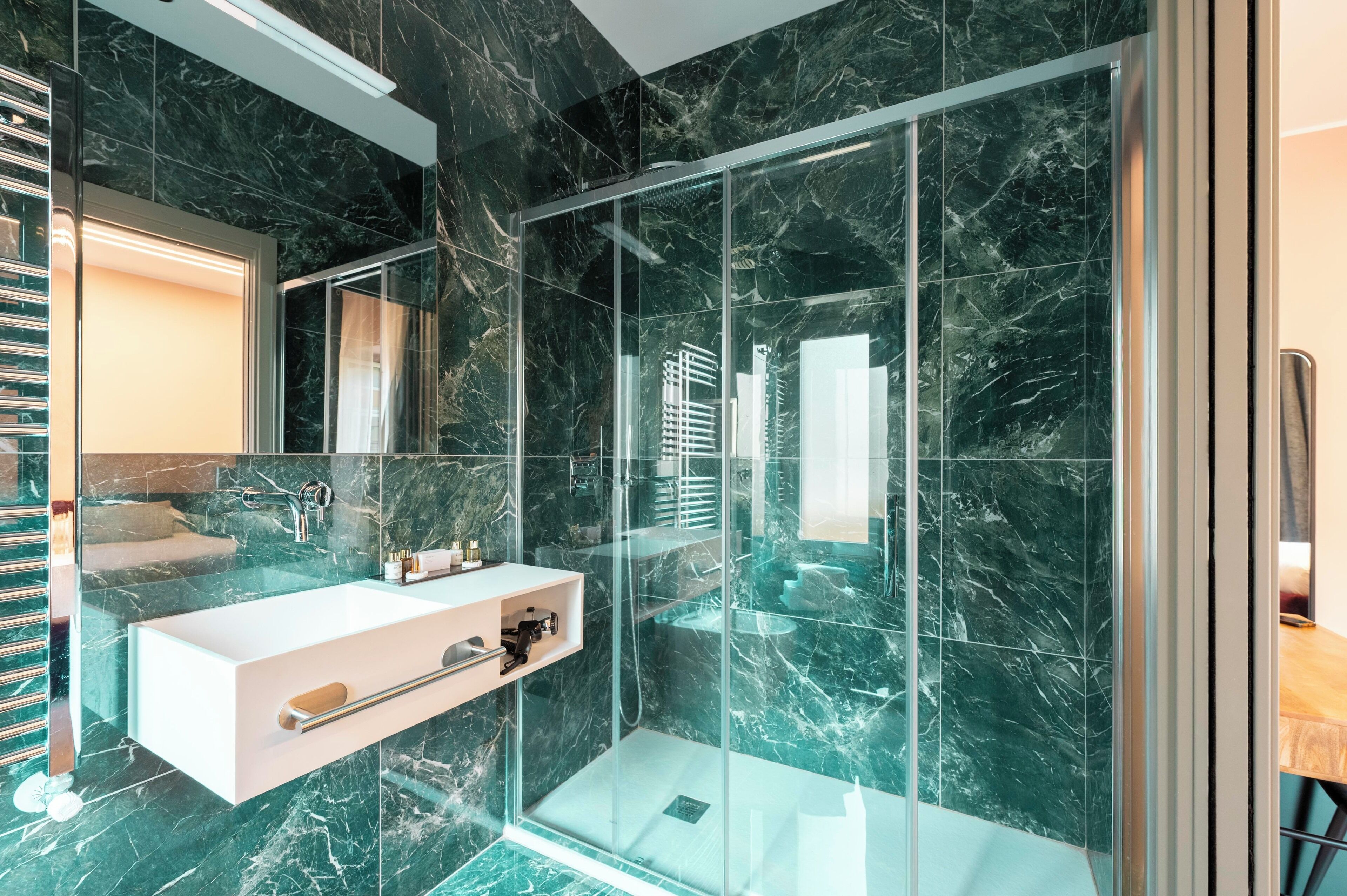 A modern bathroom with a glass-enclosed shower, a white sink, and marble flooring.