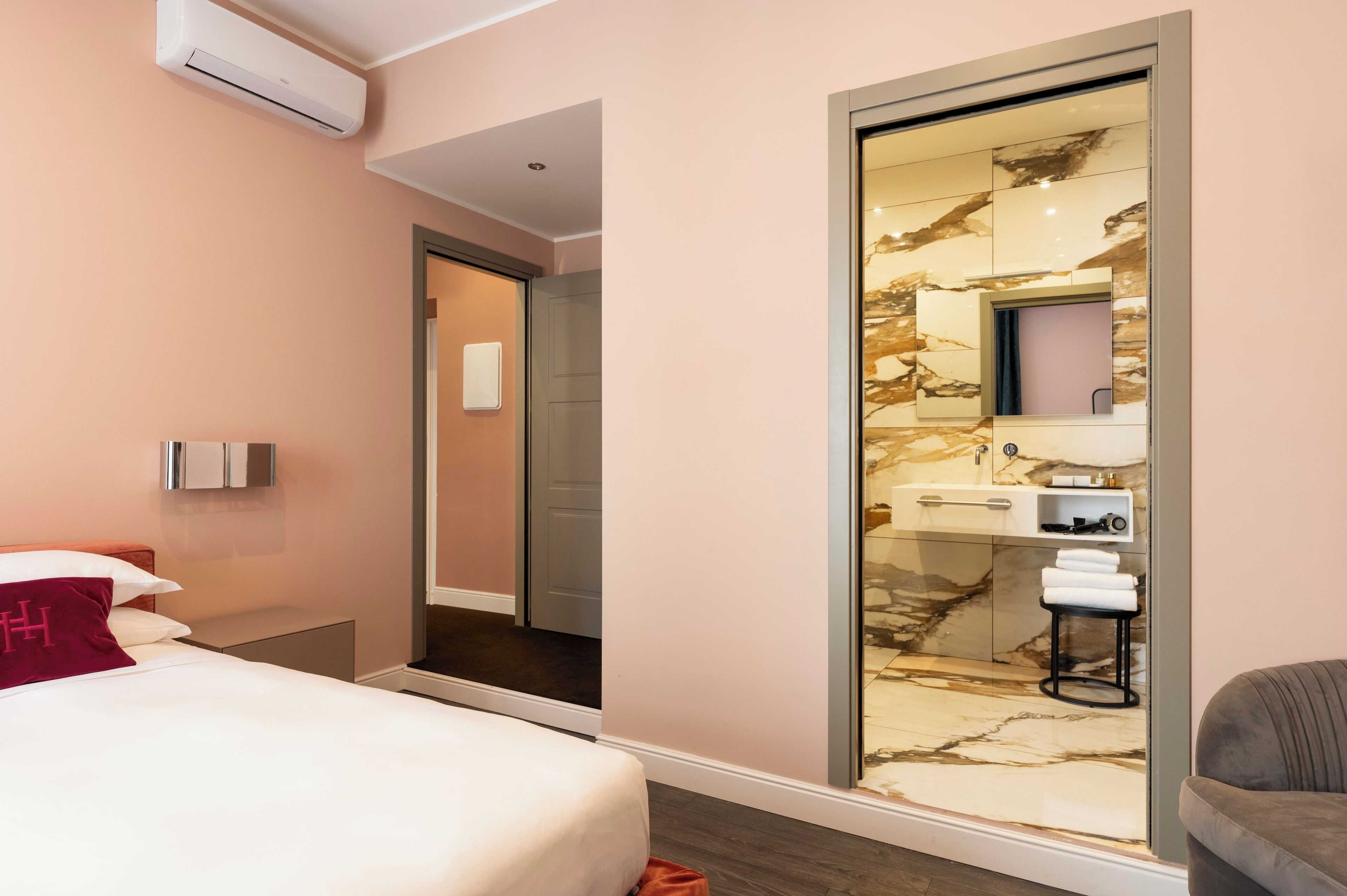 A modern hotel room with a bed, a bathroom with a marble vanity, and a sliding door leading to another room.