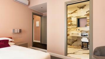 A modern hotel room with a bed, a bathroom with a marble vanity, and a sliding door leading to another room.
