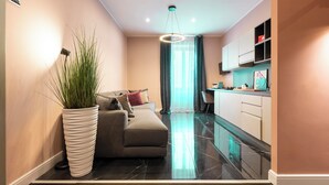 A modern living room with a sofa, a large potted plant, and a dining area with a kitchen in the background. - My Rooms in Vatican City (Rome)
