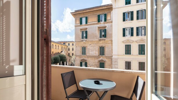 A balcony with a table and two chairs, overlooking a building with green shutters and a clear sky. - My Rooms in Vatican City (Rome)