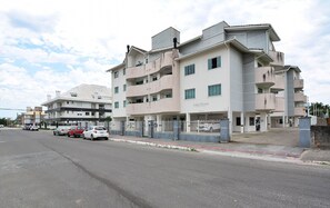 A multi-story residential building with balconies, a gated entrance, and a parking area with several cars. - Residencial João Victor - Ingleses Norte (Florianópolis)