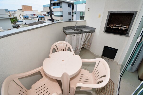 A balcony with a small kitchen area, including a sink and a grill, and a table with chairs.