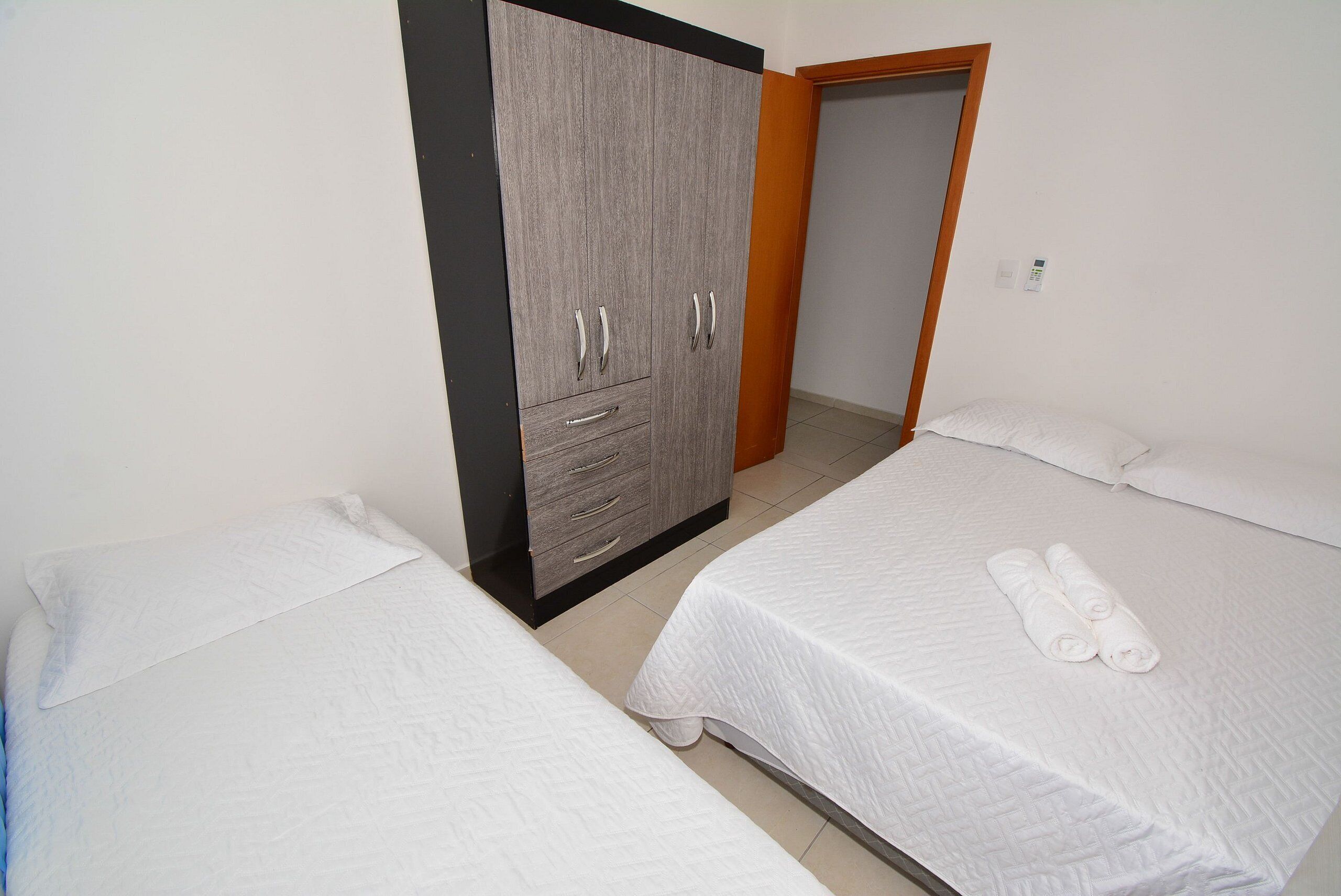 Une chambre avec deux lits, une armoire et une porte donnant sur une autre pièce.