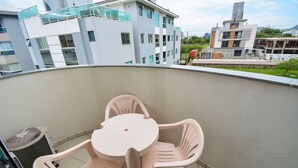Ein Balkon mit Tisch und Stühlen, einem Mülleimer und Blick auf moderne Gebäude im Hintergrund.