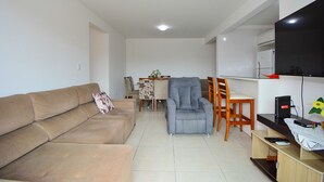 Una sala de estar con un sofá, una silla, una mesa de comedor con sillas, un televisor y un mueble bajo.