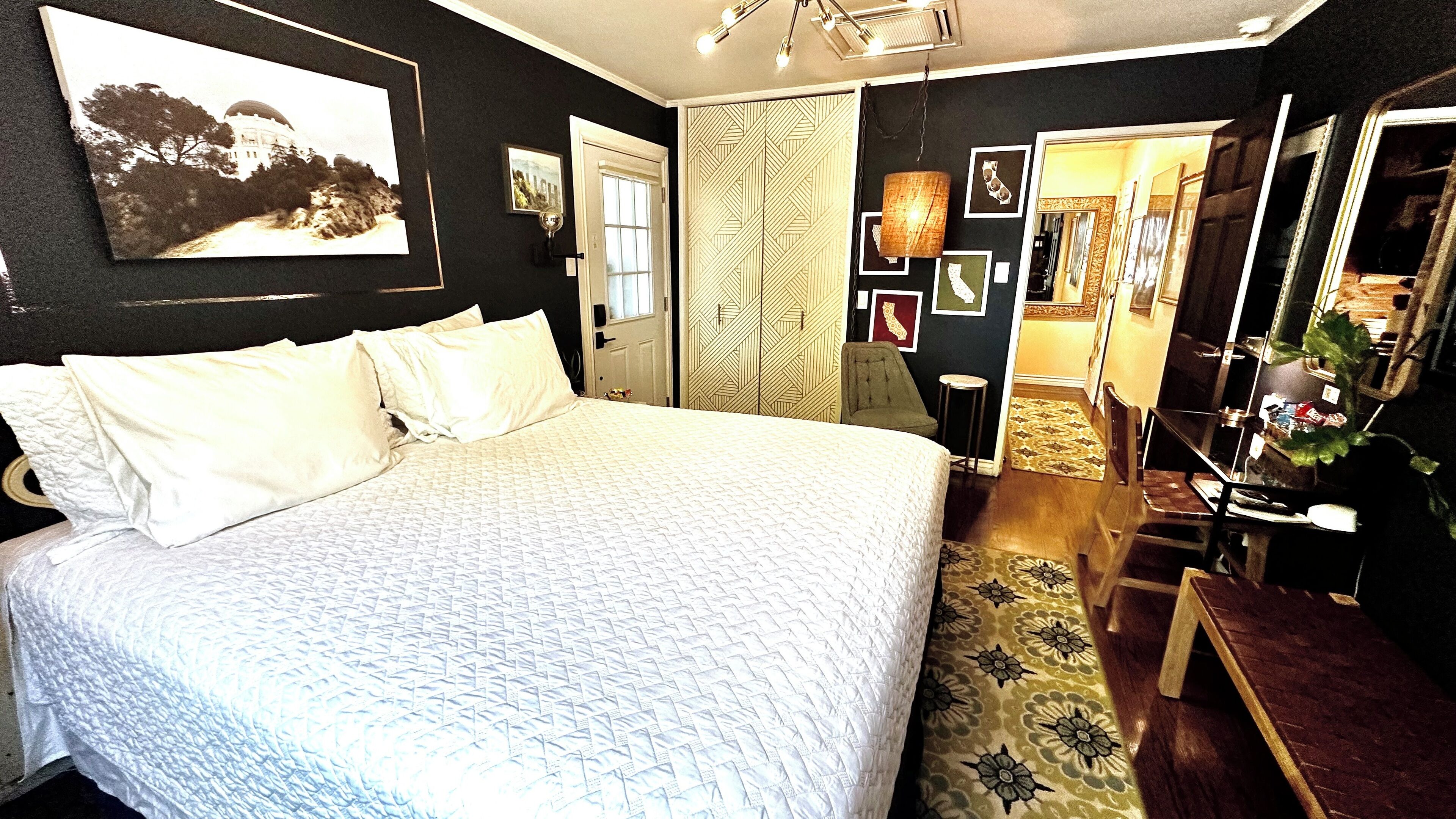 A bedroom with a large bed, a wardrobe, a mirror, and a door leading to another room.