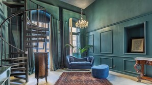 A room with a spiral staircase, a blue sofa, a wooden table, and a chandelier. - House of W (Valletta)