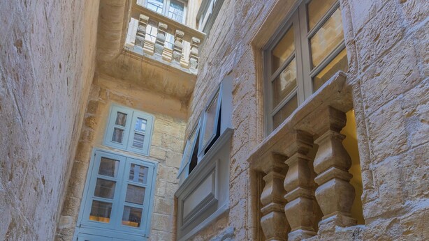A narrow alleyway with stone walls and a small window with a wooden shutter. - House of W (Valletta)