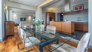 A modern kitchen with wooden cabinets, a central island, and a dining area with glass-top table and cushioned chairs. - House of W (Valletta)